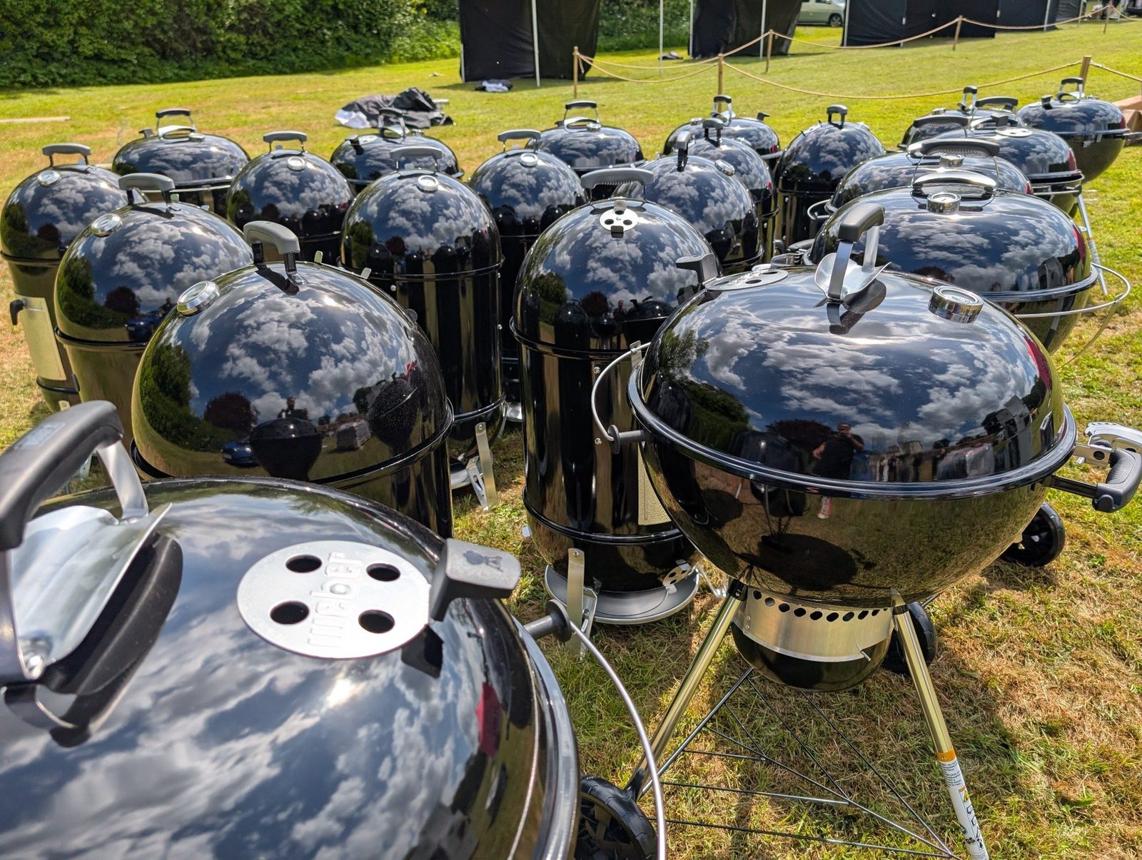 A field of black Weber kettle grills reflecting the sky at a competition