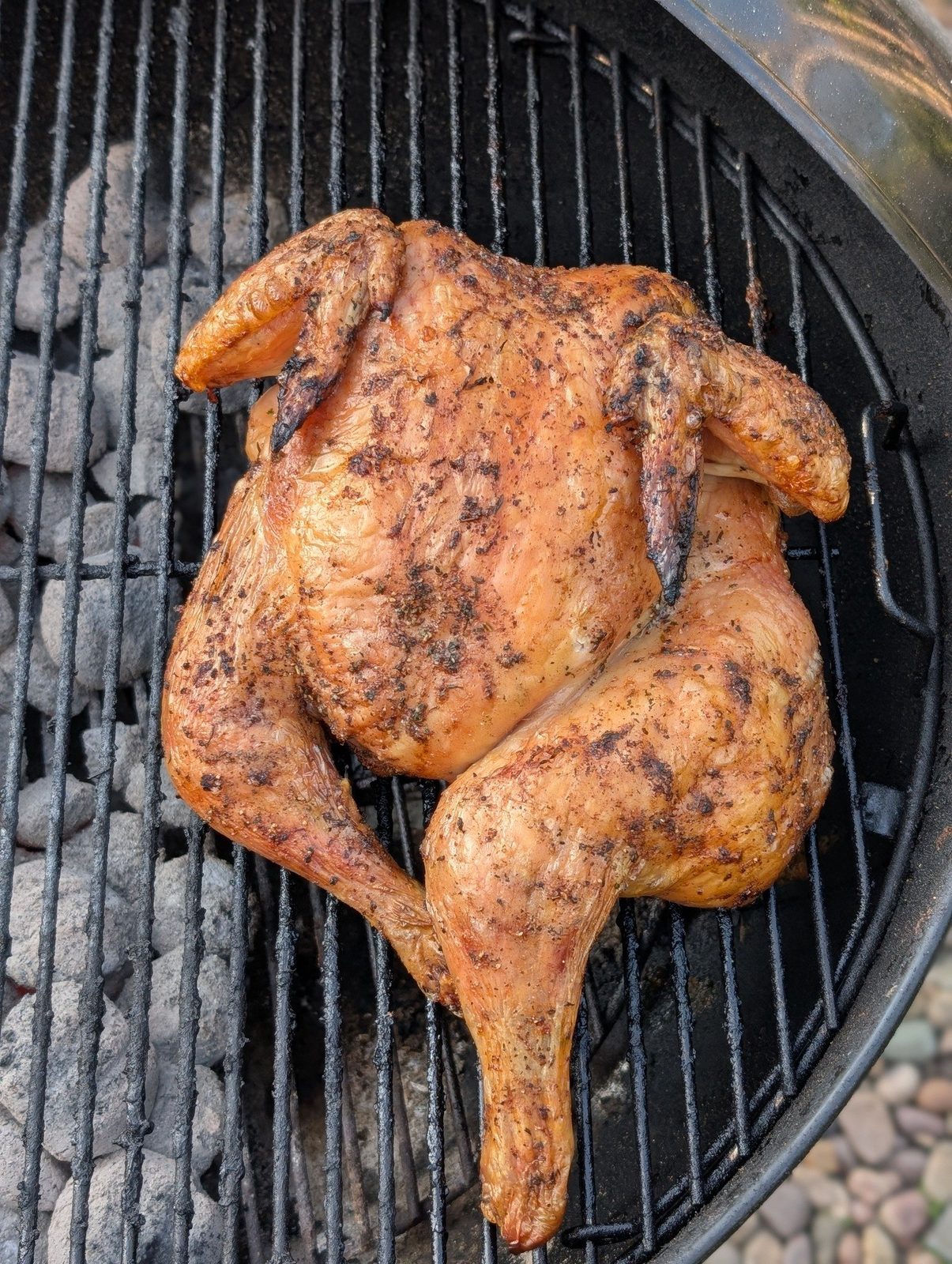 A whole chicken cooking on a kettle grill