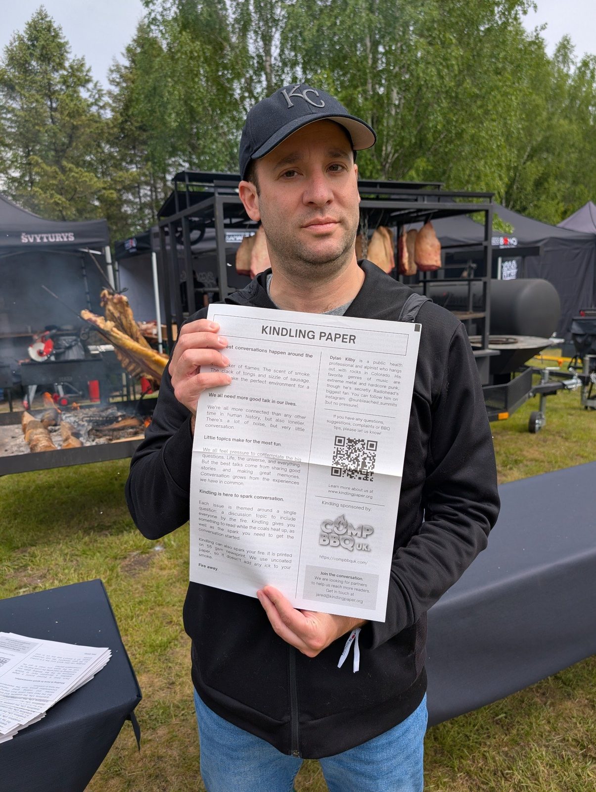 Jared holding an open copy of Kindling newspaper beside a barbecue